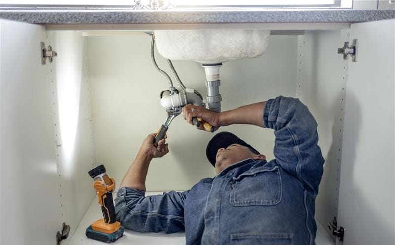 Plumber repairing pipes beneath a bathroom sink in Campbell